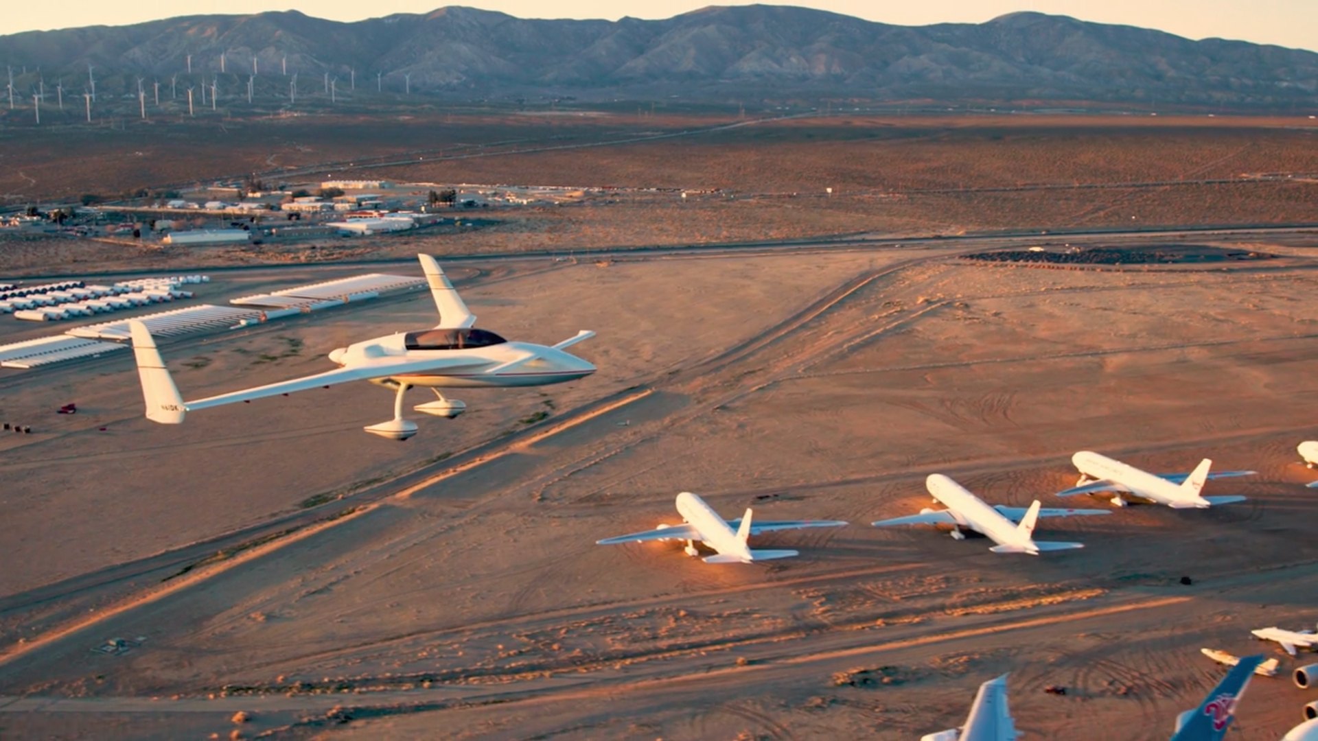 Air-to-air shot of a canard aircraft flying over the Mojave aircraft boneyard at golden hour